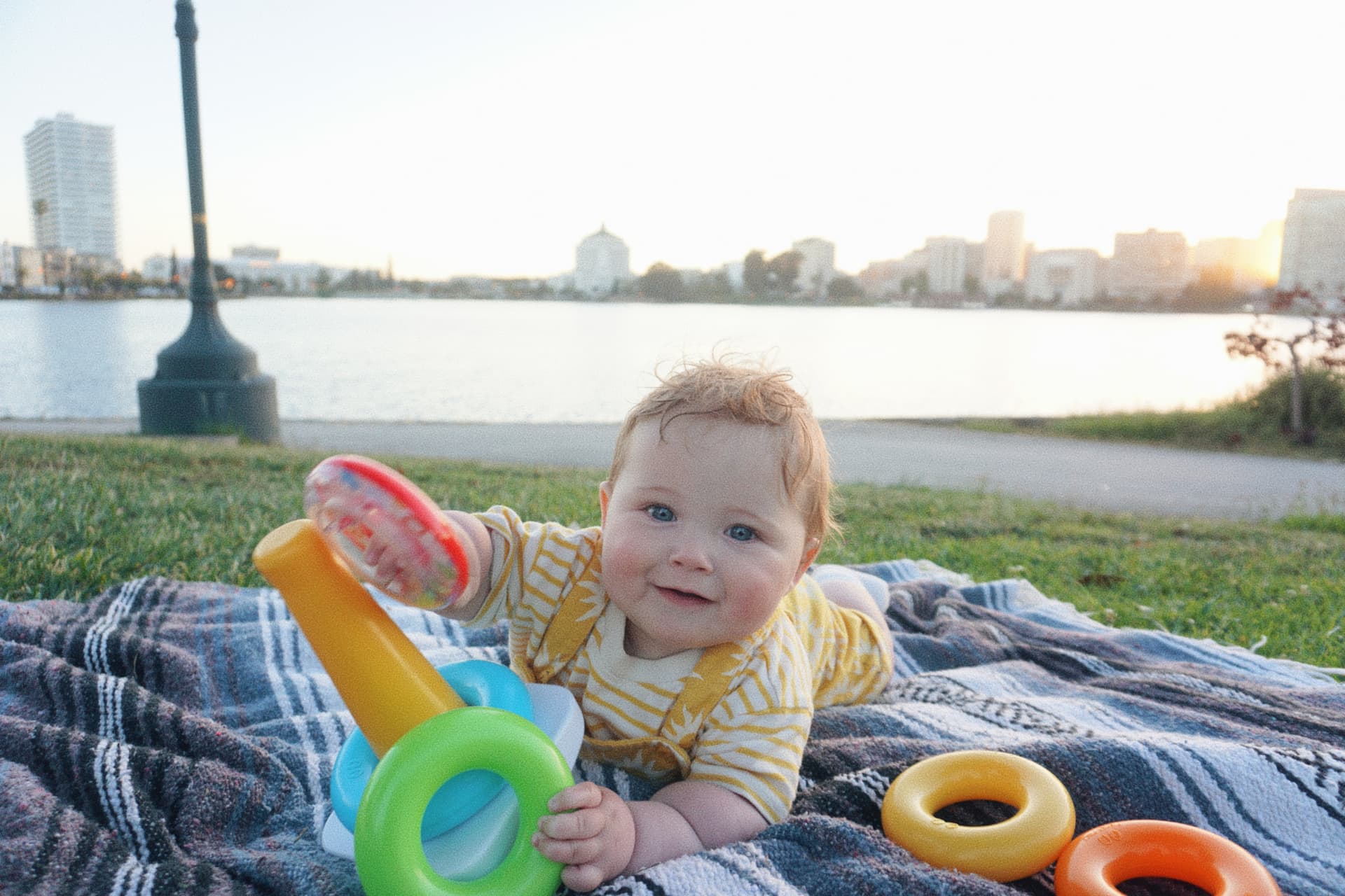 The Espicha-Blumenstein baby playing with stacking rings on a blanket by Lake Merritt at sunset
