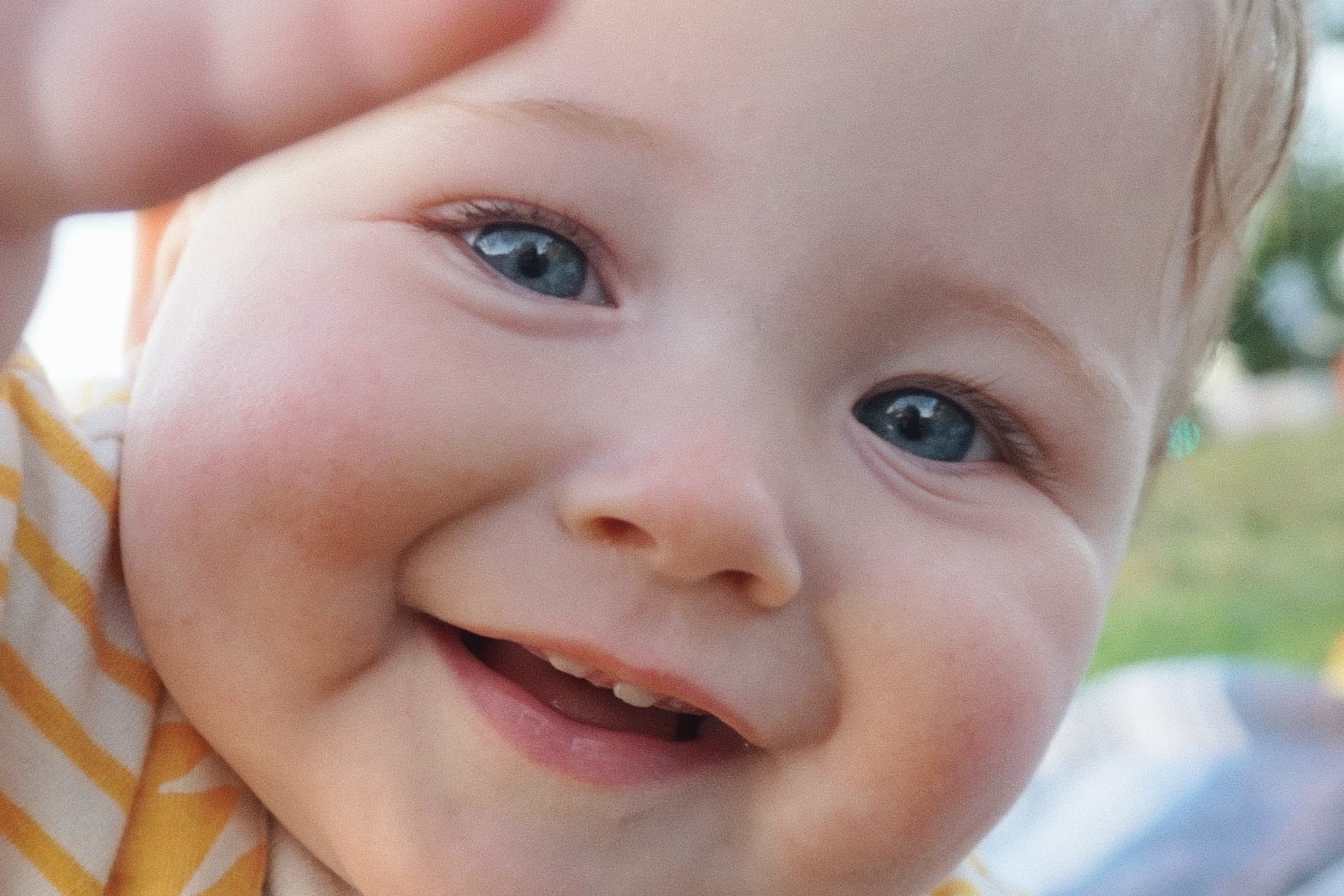 Close-up of the Espicha-Blumenstein baby grinning with bright blue eyes in golden afternoon light