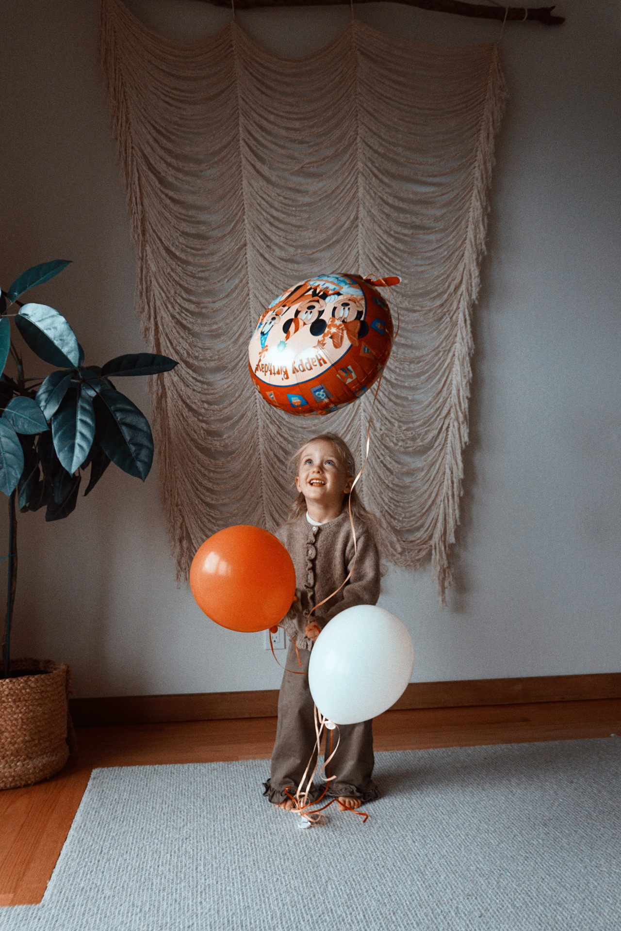 The Fleischmann daughter smiling up at a birthday balloon while holding orange and white balloons at home