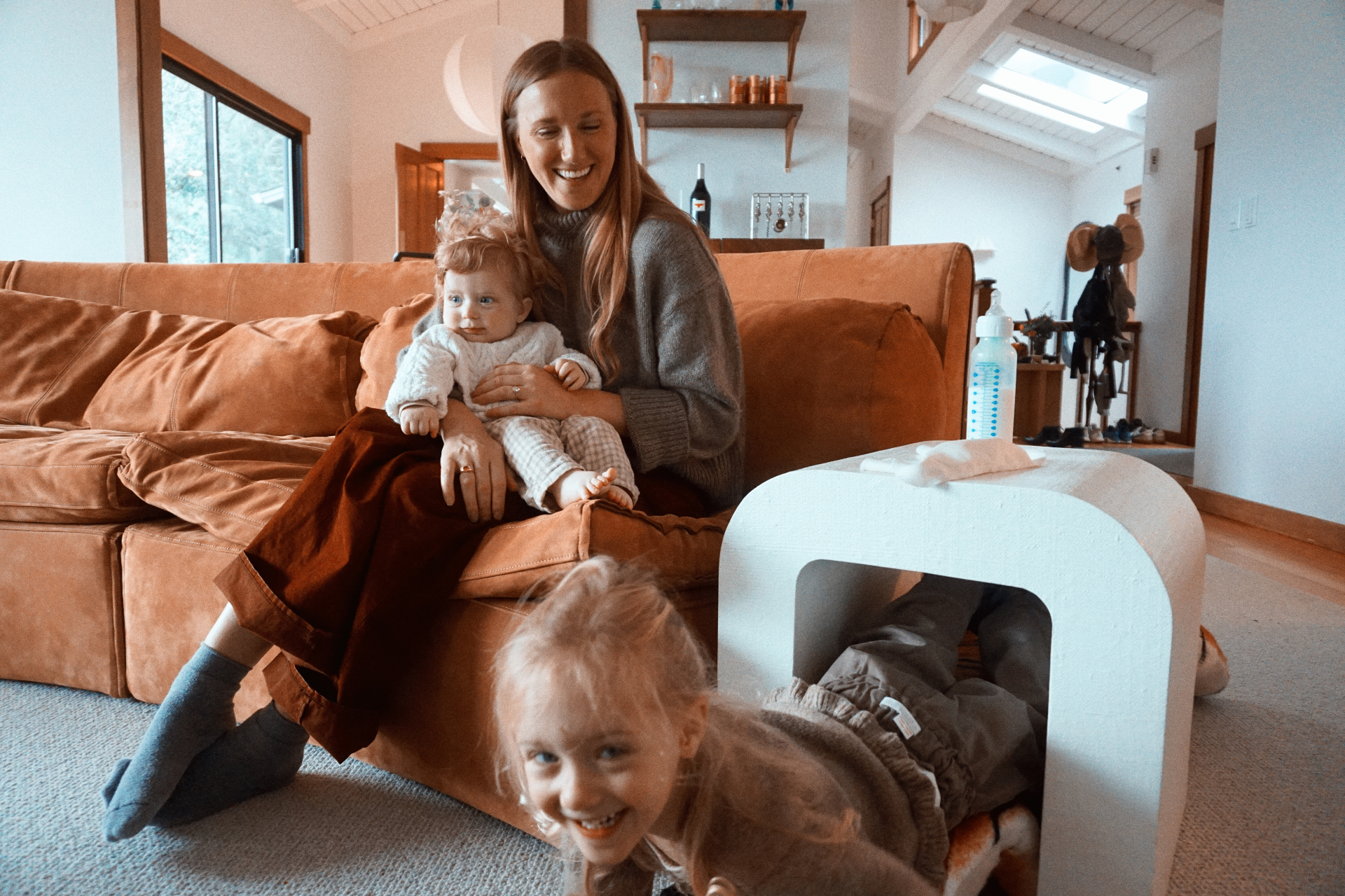 The Fleischmann mother laughing with her baby on the couch while her daughter plays on the floor