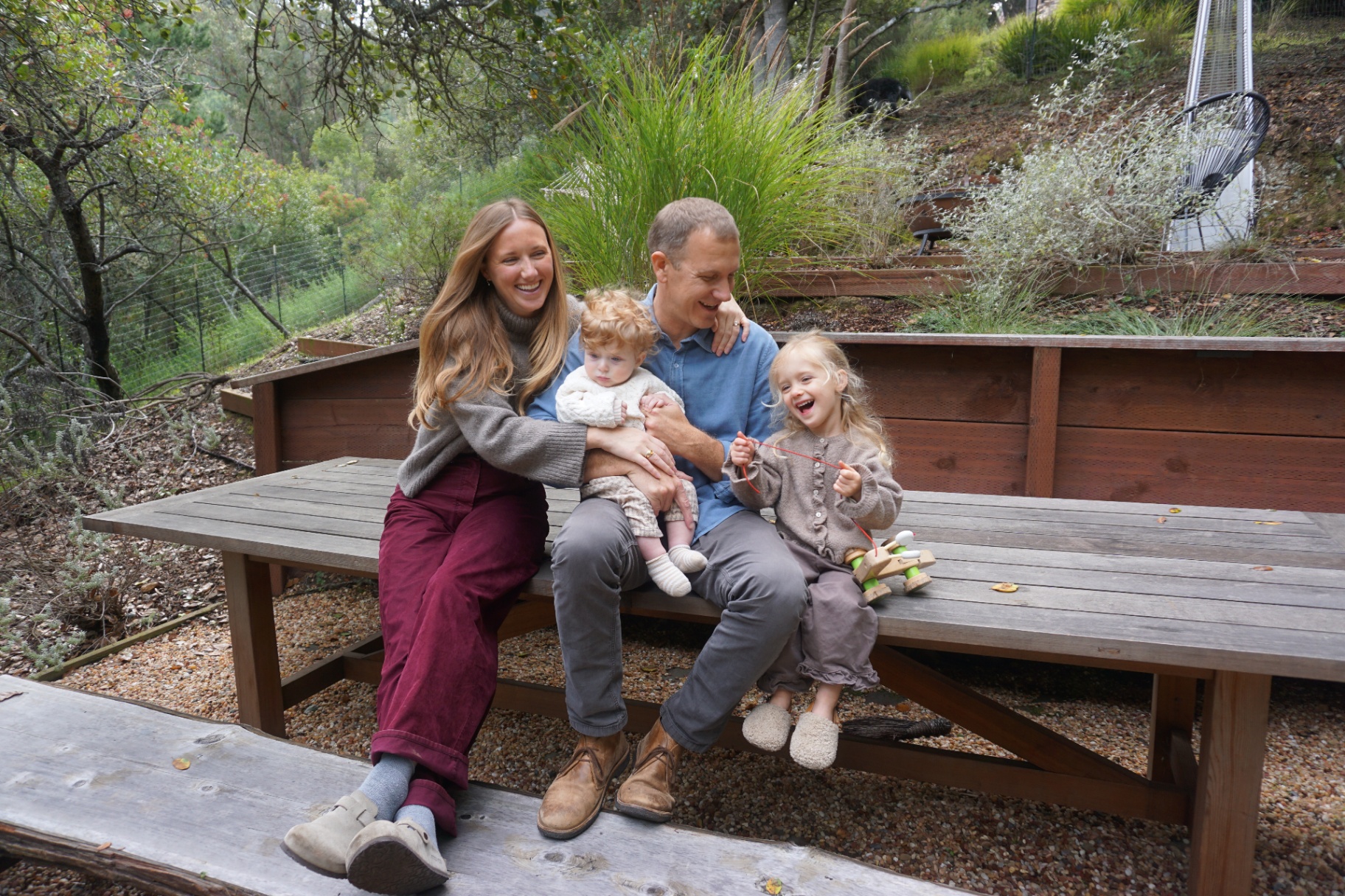 The Fleischmann family laughing together on a picnic table outdoors surrounded by greenery