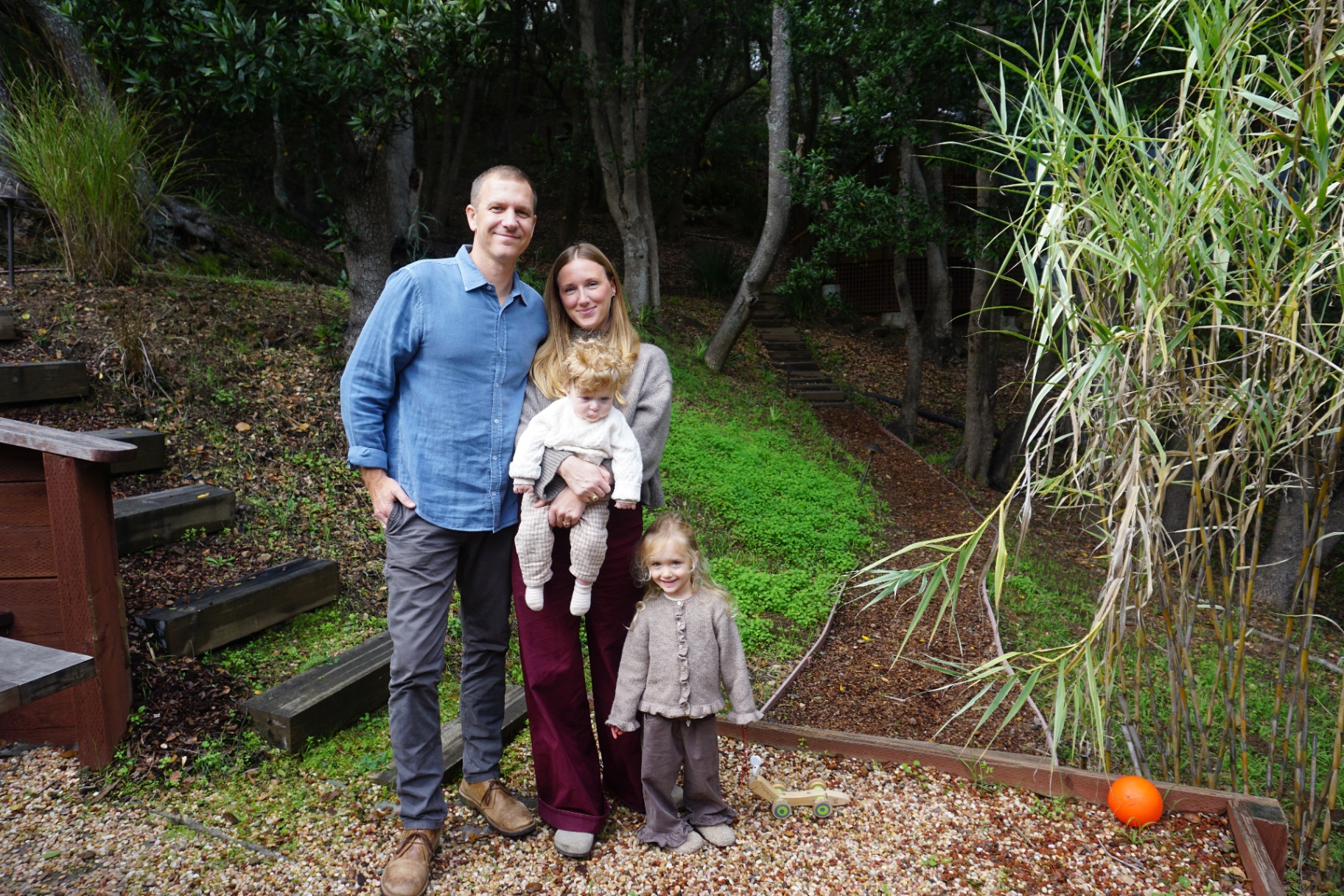 The Fleischmann family of four standing together in a wooded garden with bamboo and a small wooden cart