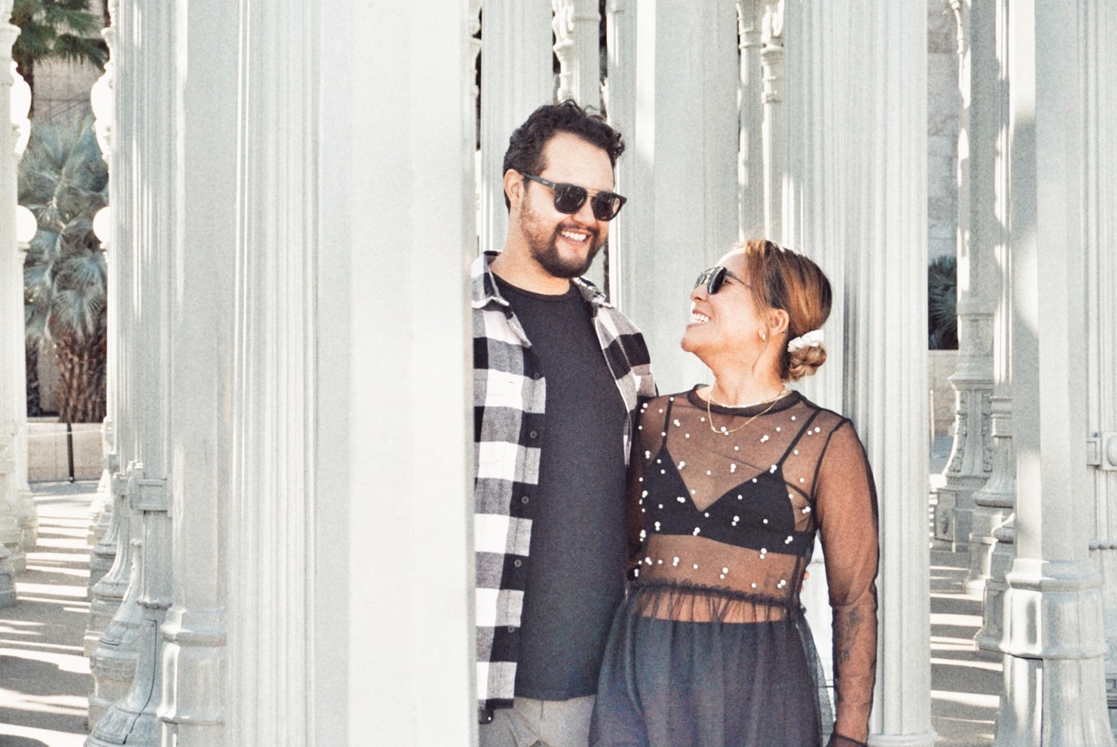 Engaged couple smiling at each other between sunlit columns