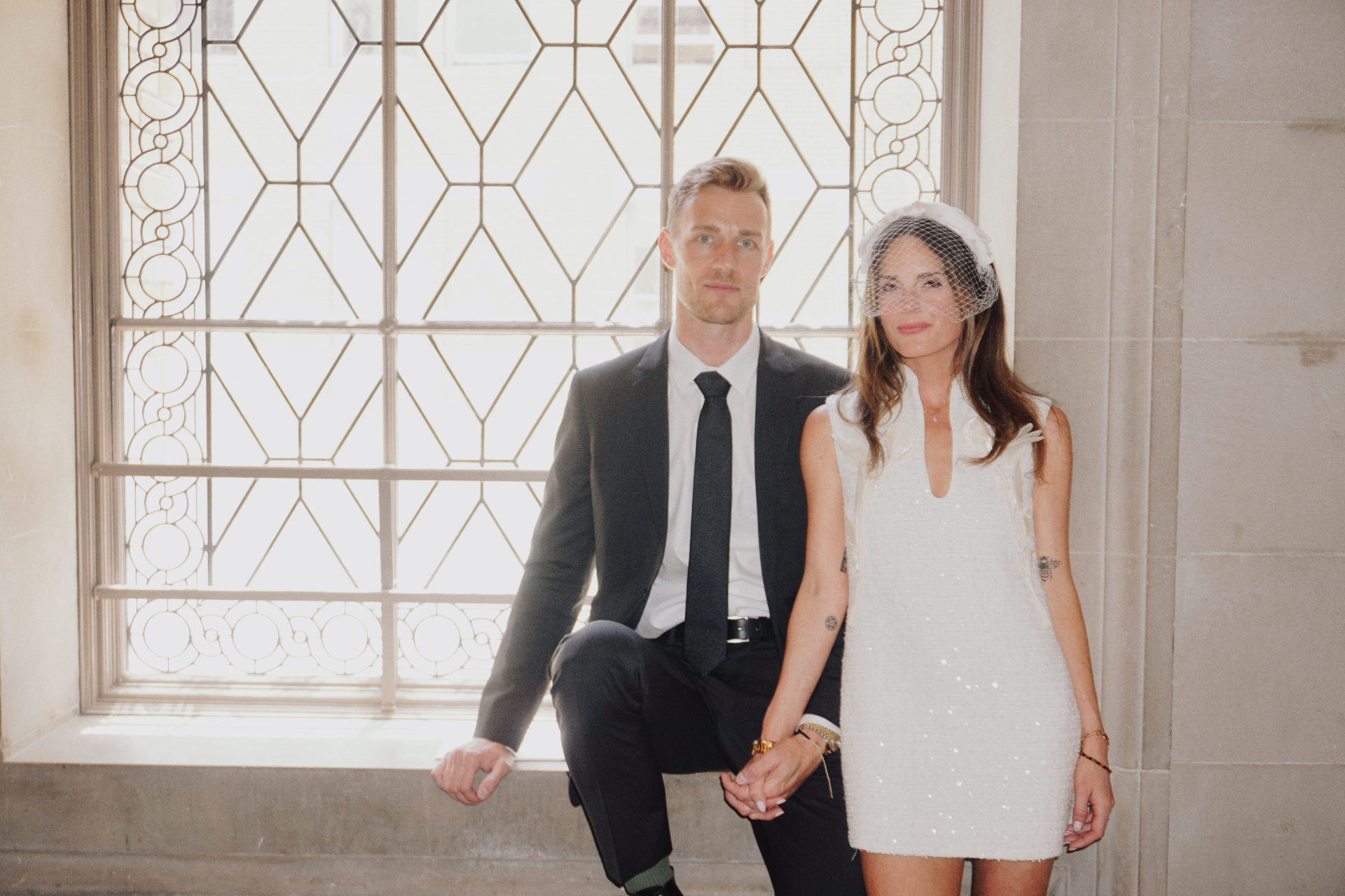 Maggie and Jono seated together by a bright window during their City Hall photoshoot