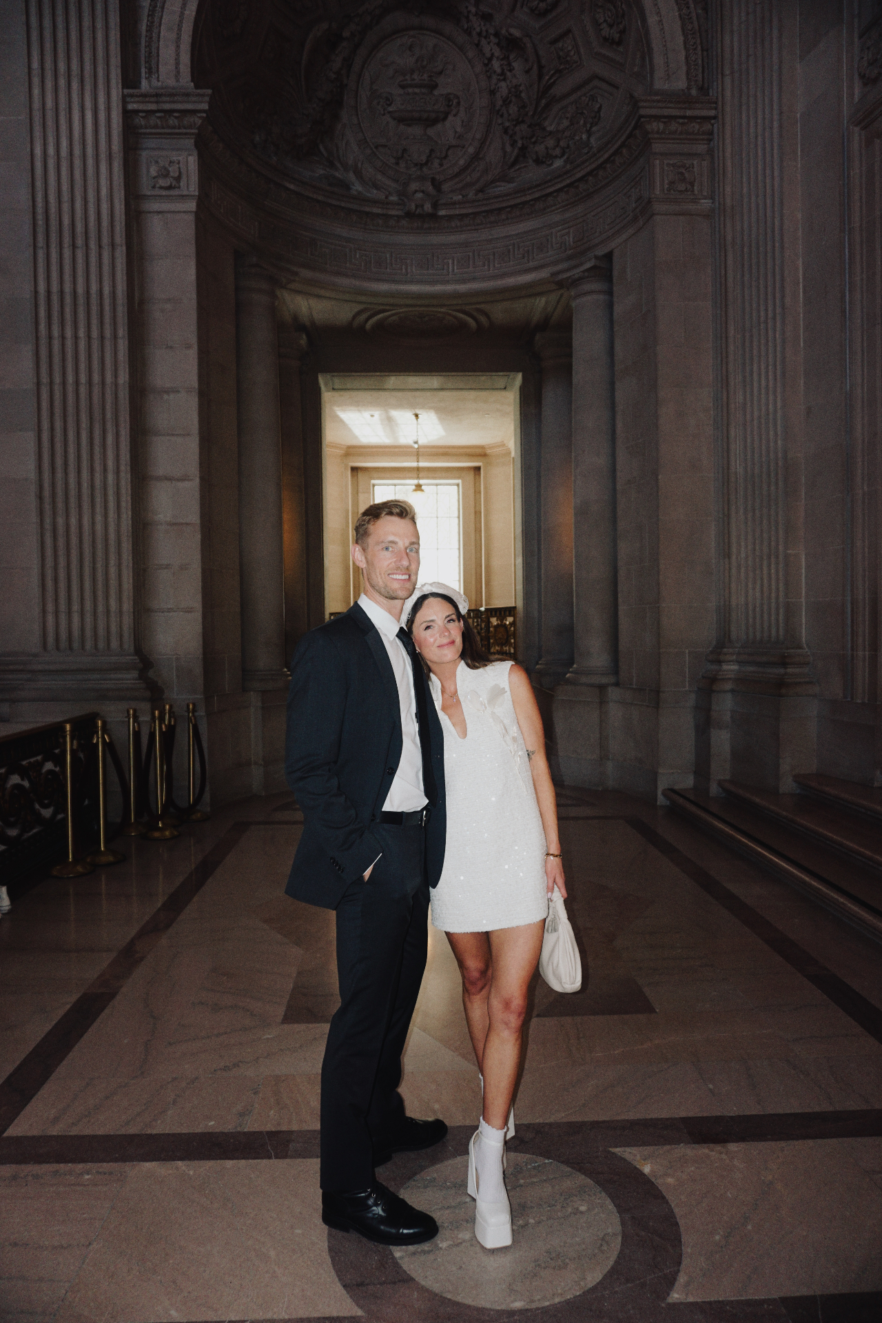 Maggie and Jono posing together in a grand columned hallway at San Francisco City Hall