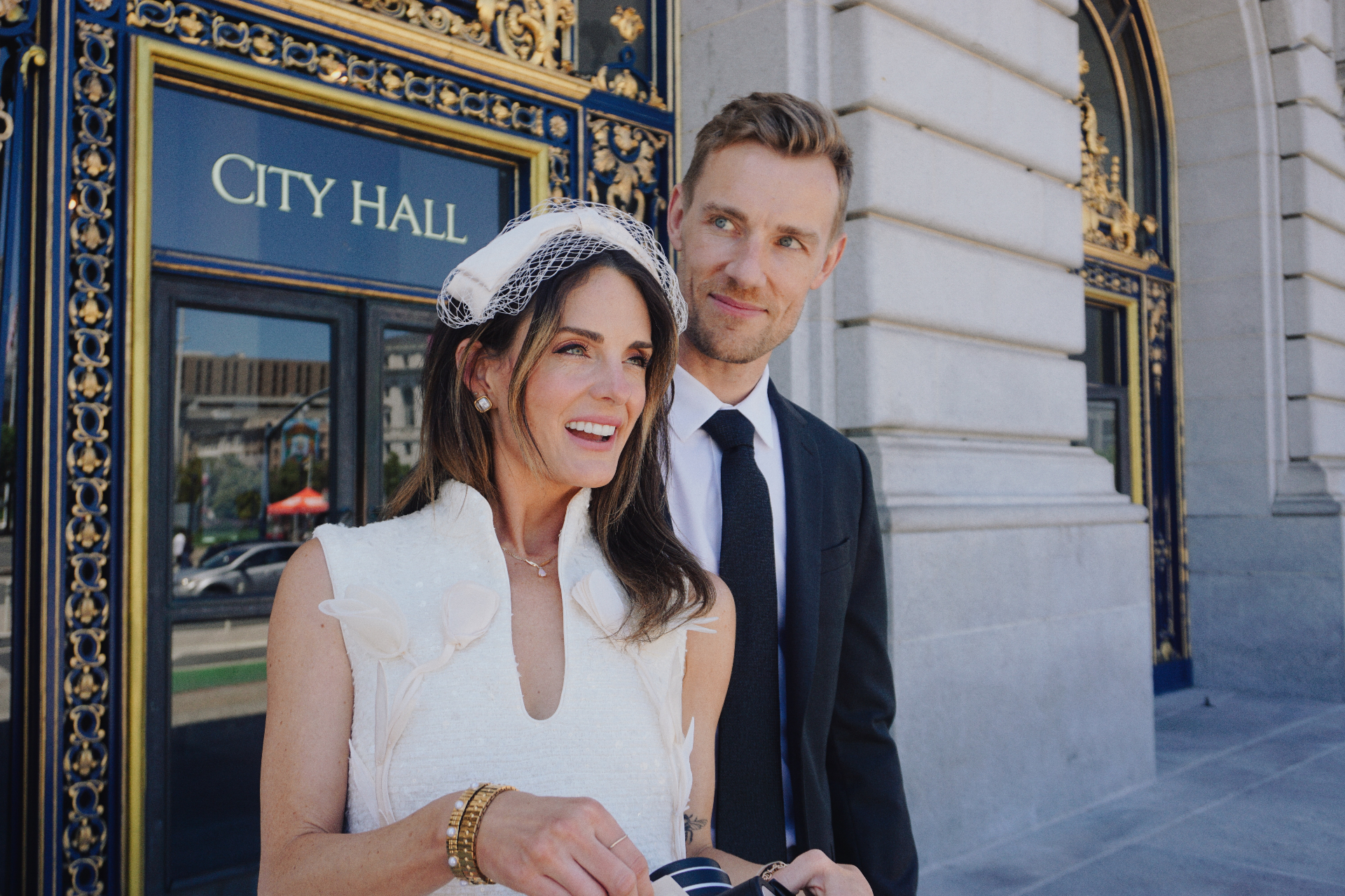 Maggie and Jono smiling together outside the gilded City Hall entrance in San Francisco