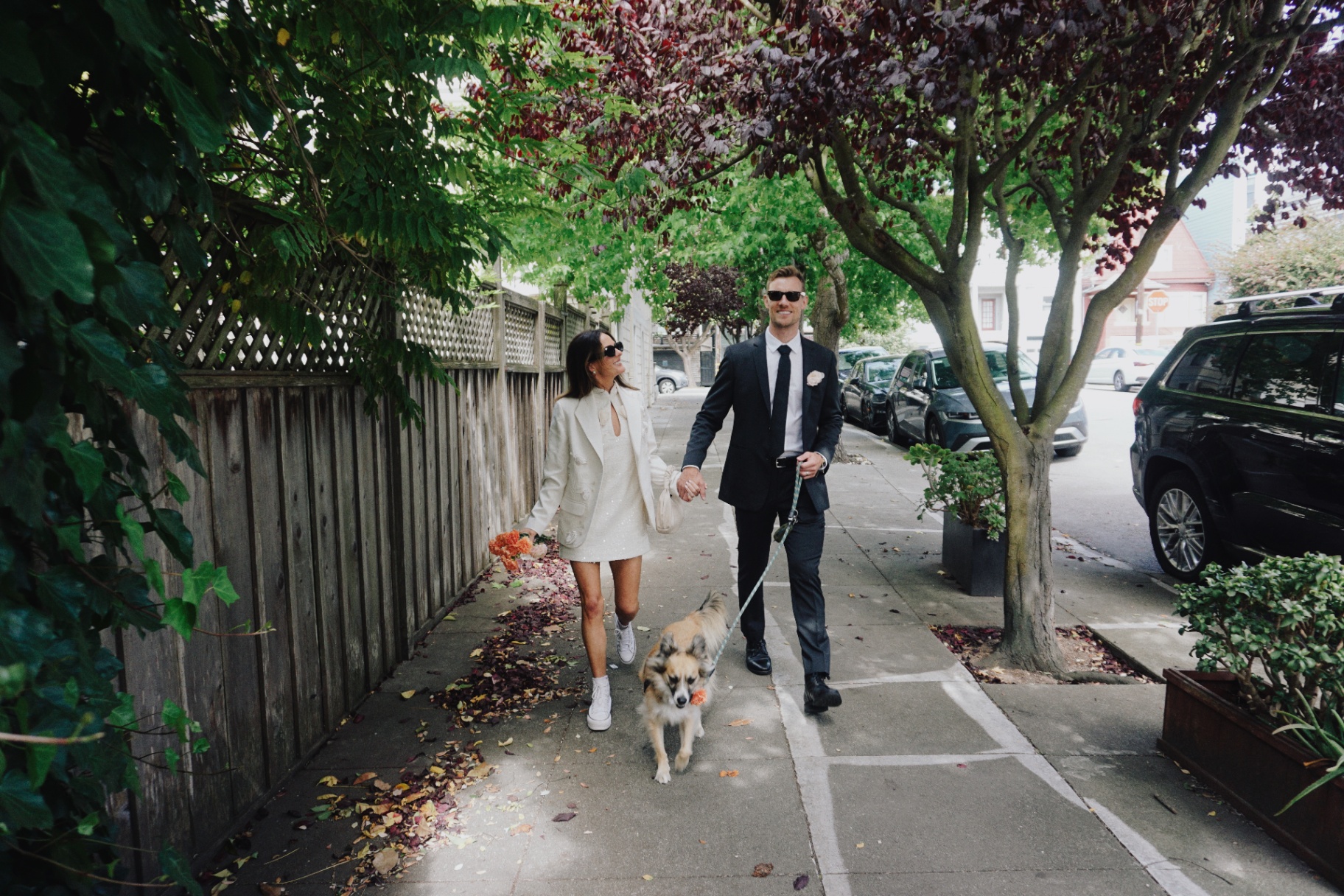 Maggie and Jono walking their dog down a tree-lined San Francisco sidewalk after their City Hall ceremony