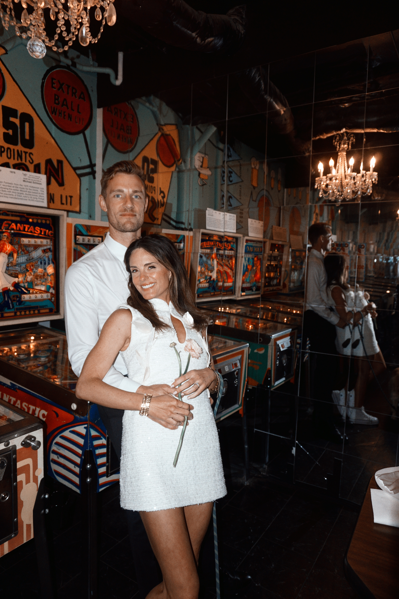 Maggie and Jono embracing among vintage pinball machines and chandeliers after their City Hall ceremony