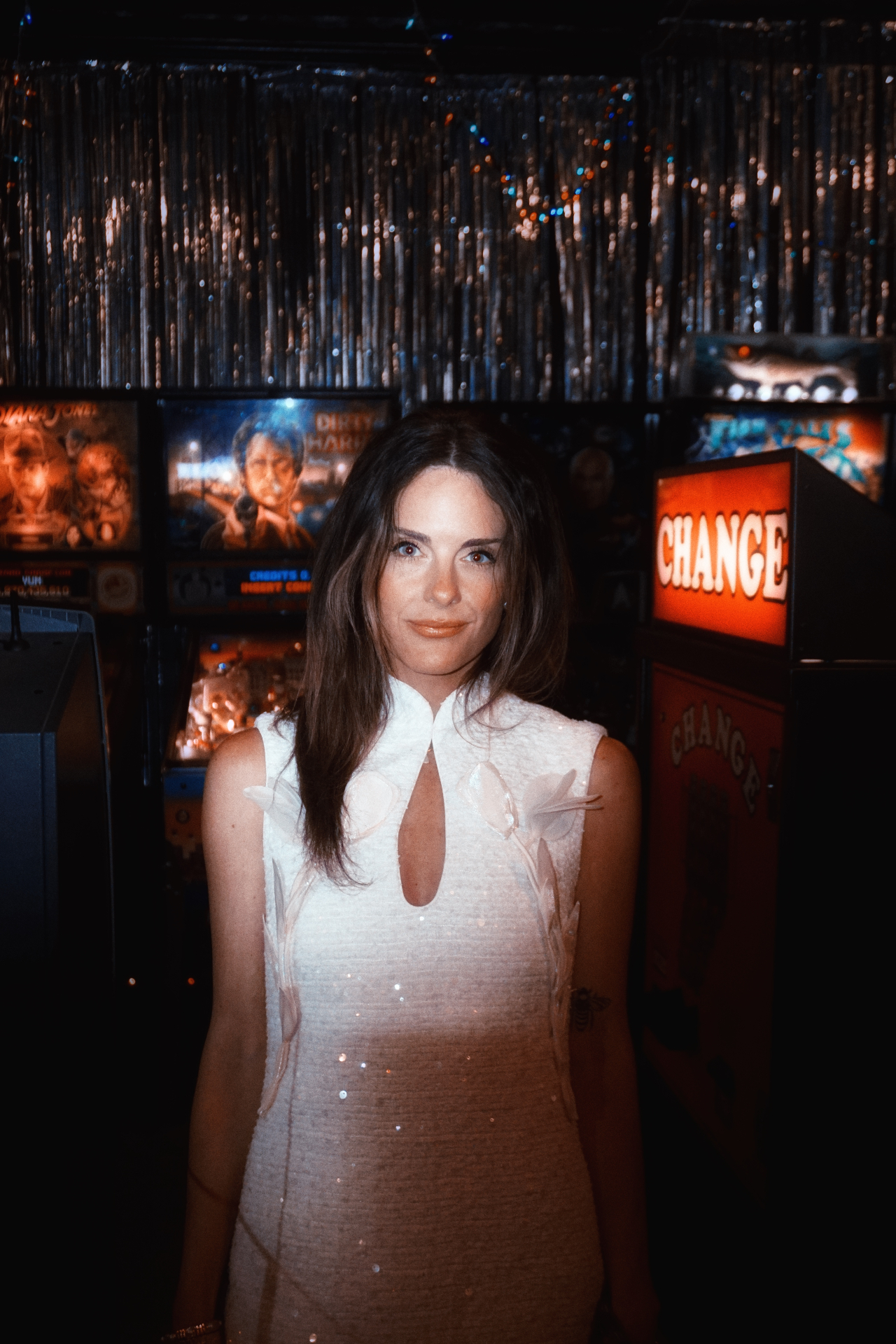 Maggie smiling in her wedding dress under shimmering tinsel in a pinball arcade