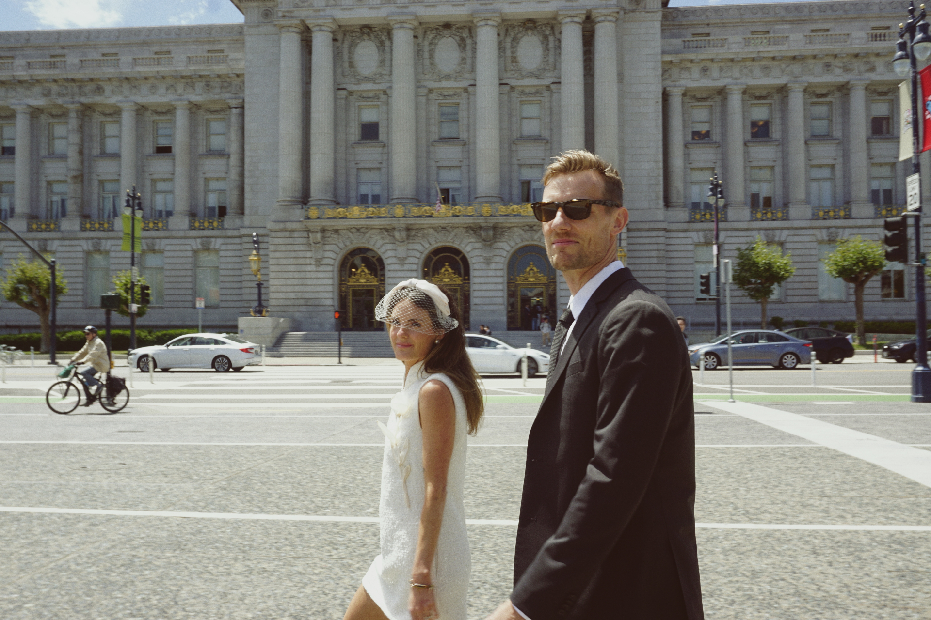Maggie and Jono walking across the street in front of San Francisco City Hall on a sunny day