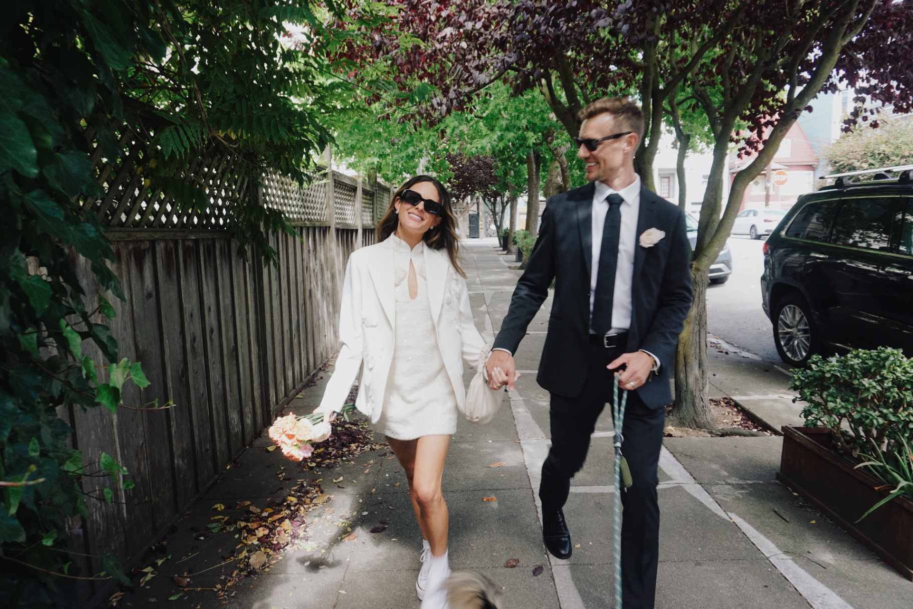 Maggie and Jono holding hands while walking their dog down a tree-lined San Francisco sidewalk