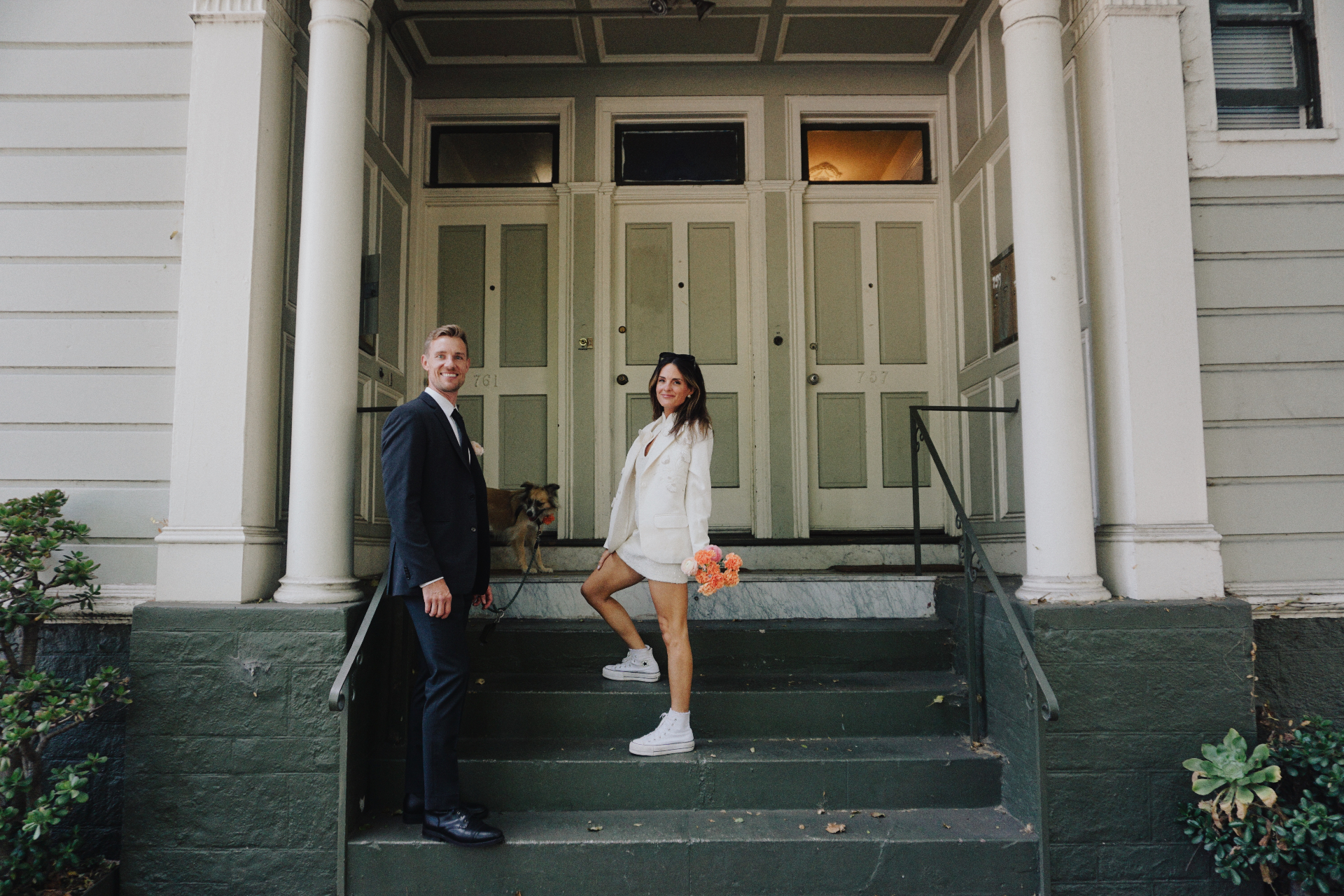 Maggie and Jono posing playfully with their dog on the front steps of a San Francisco Victorian home