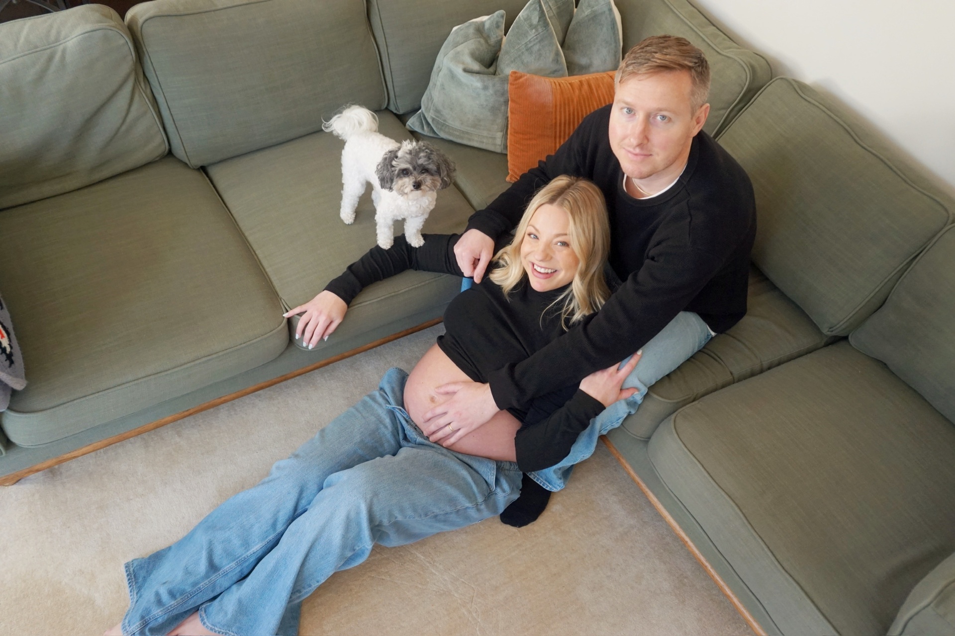The Parson parents sitting together on a green sectional sofa with their small dog during the maternity photoshoot