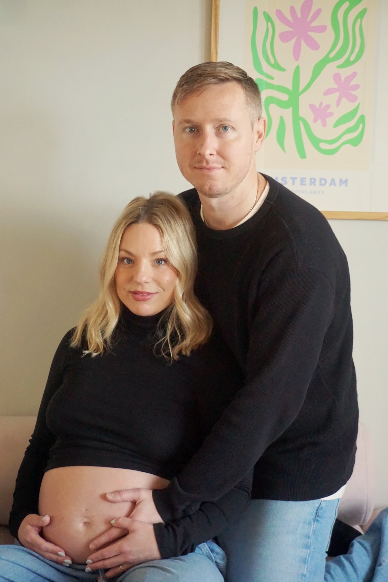 The Parson parents seated closely together in front of a framed Amsterdam botanical print during their maternity photoshoot