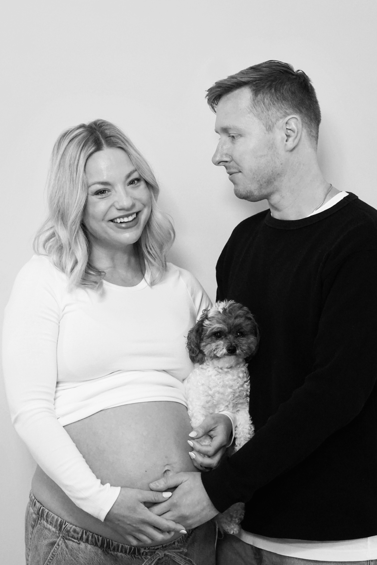 Black and white maternity portrait of The Parson parents holding their small dog between them