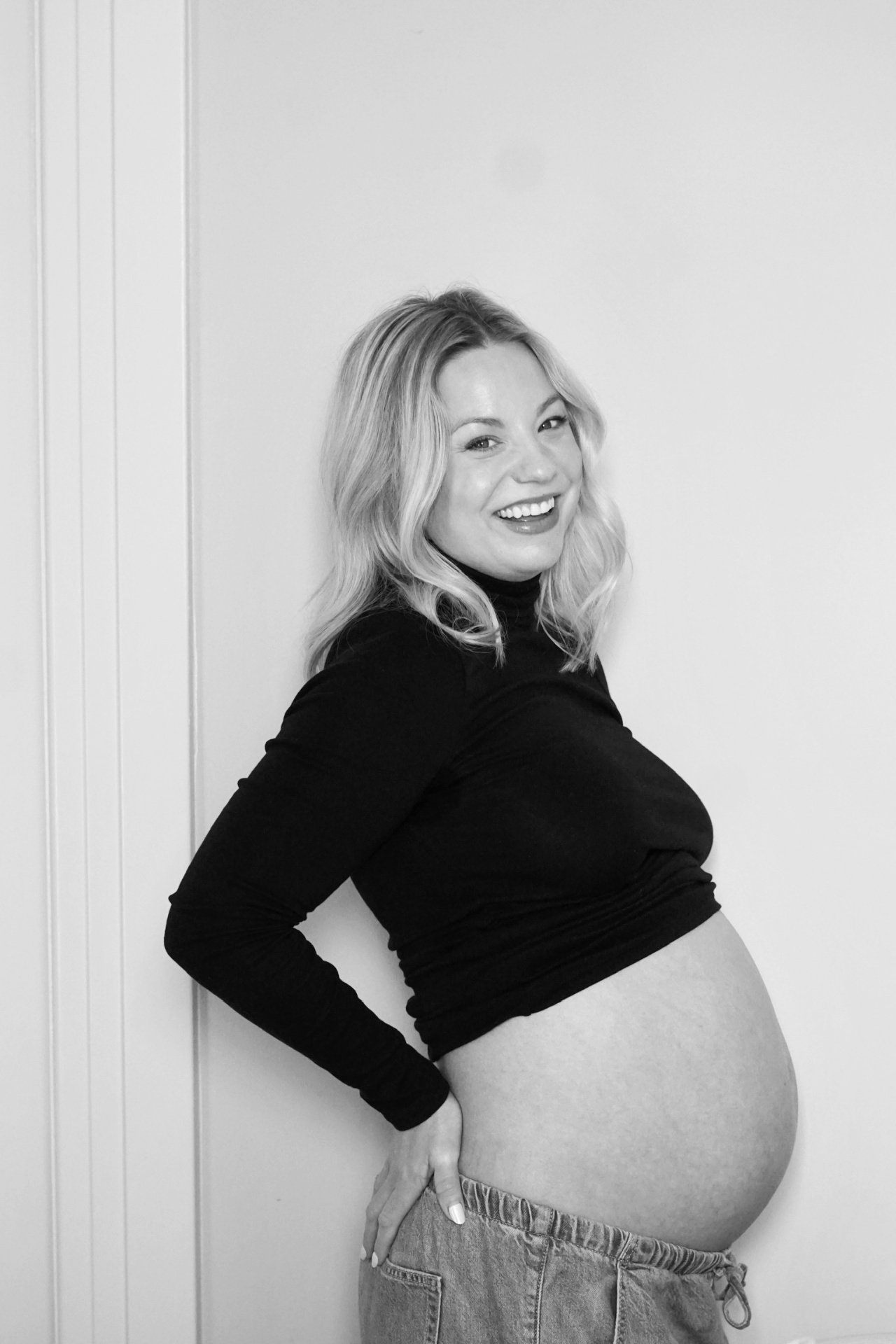 Black and white profile portrait of The Parson mother smiling in a black turtleneck cradling her baby bump