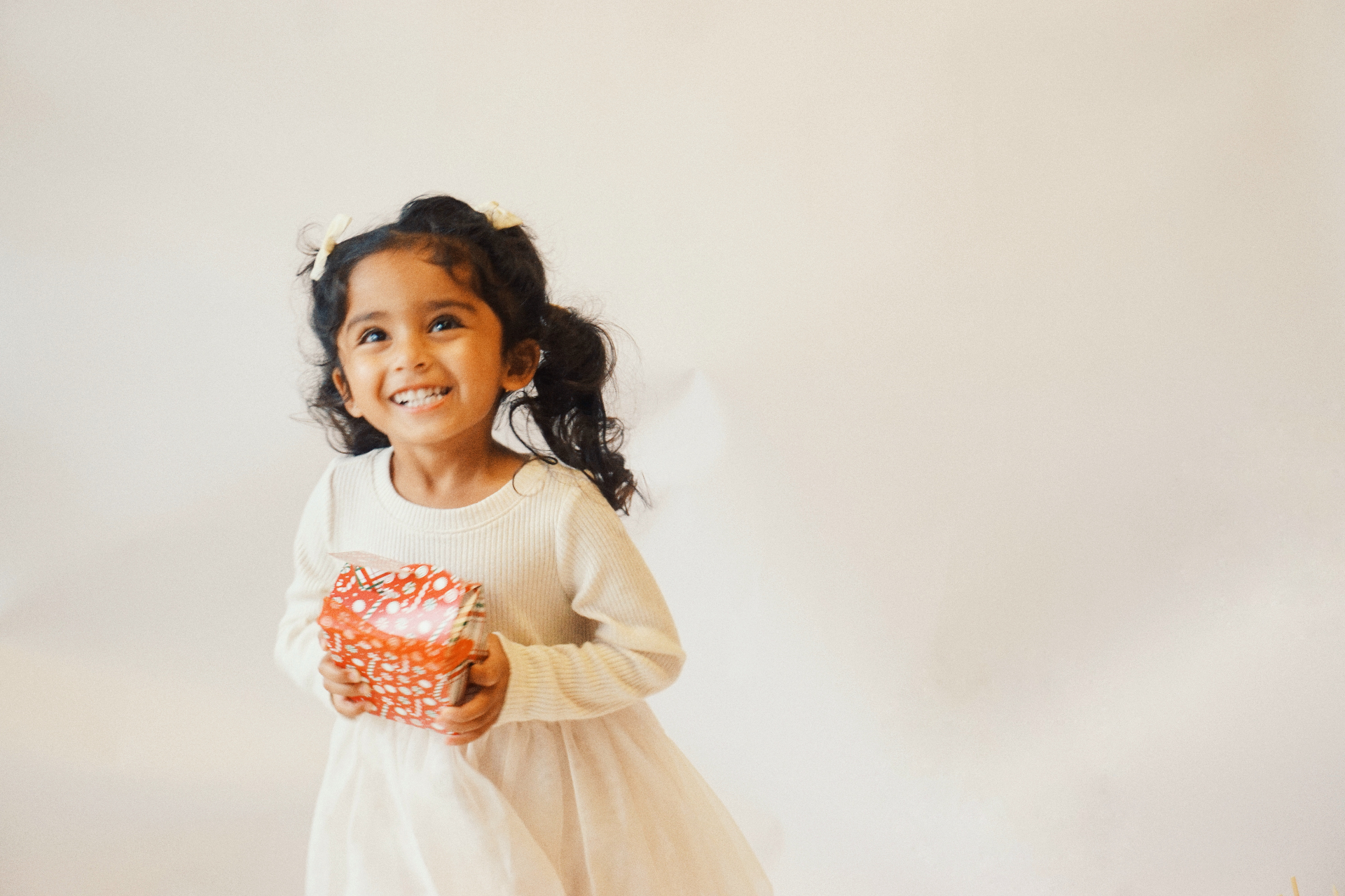 The Ramachandran daughter laughing joyfully while holding a wrapped gift in a cream dress