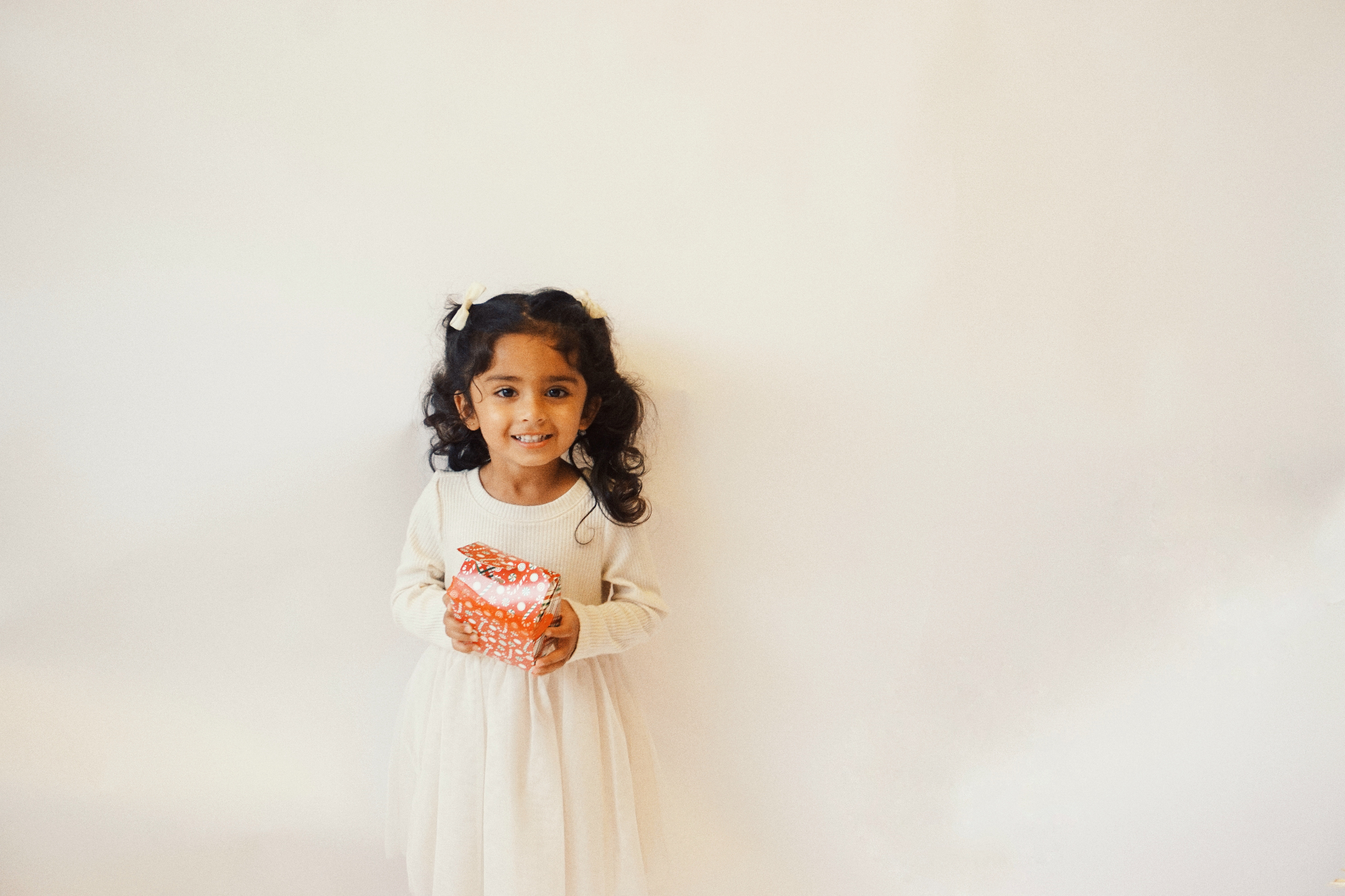 The Ramachandran daughter smiling sweetly while holding a wrapped gift against a soft neutral backdrop