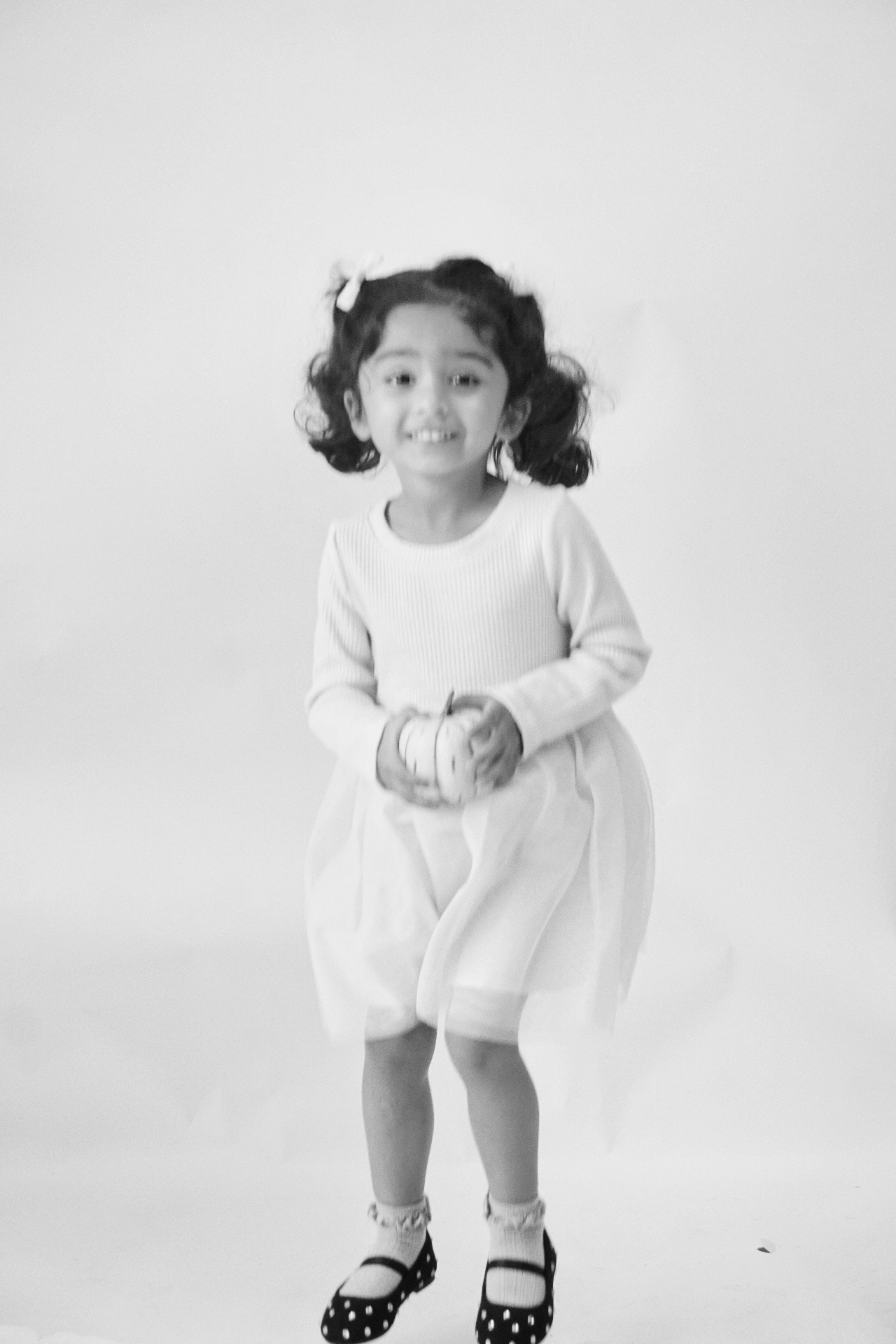 Black and white portrait of The Ramachandran daughter playfully jumping while holding a small pumpkin