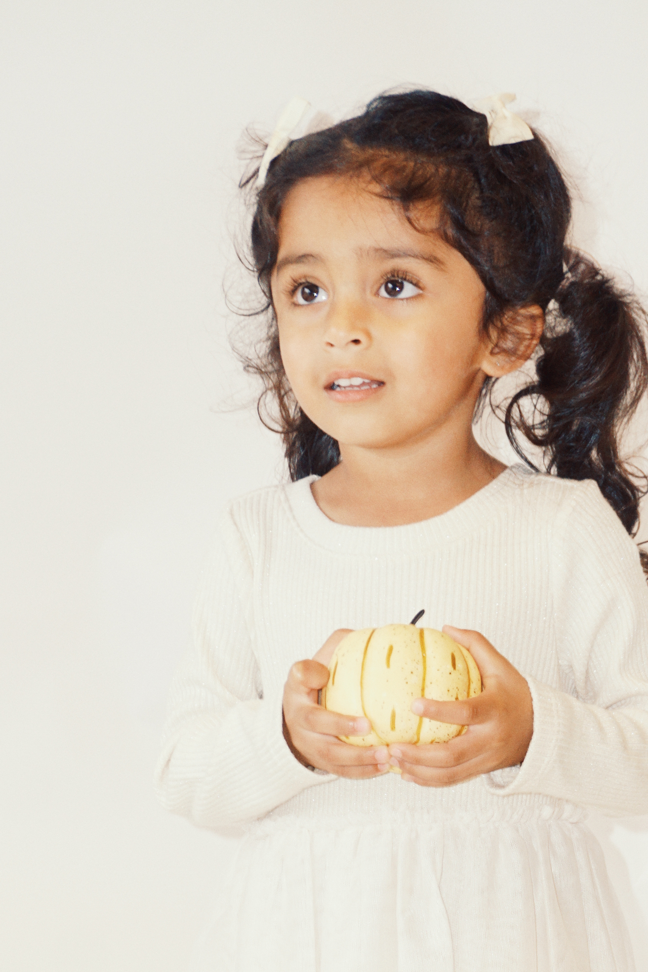 Close portrait of The Ramachandran daughter in pigtails holding a small yellow pumpkin