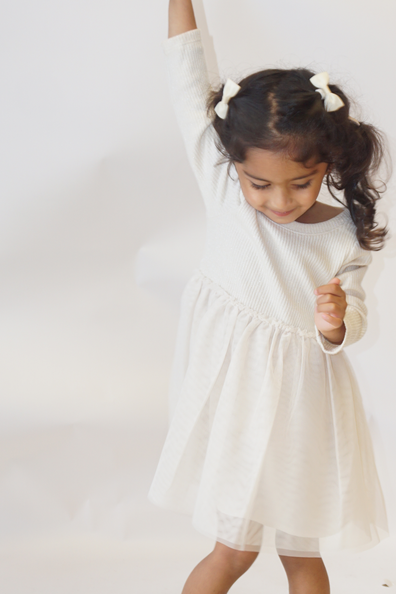 The Ramachandran daughter twirling with one arm raised in a cream tulle dress