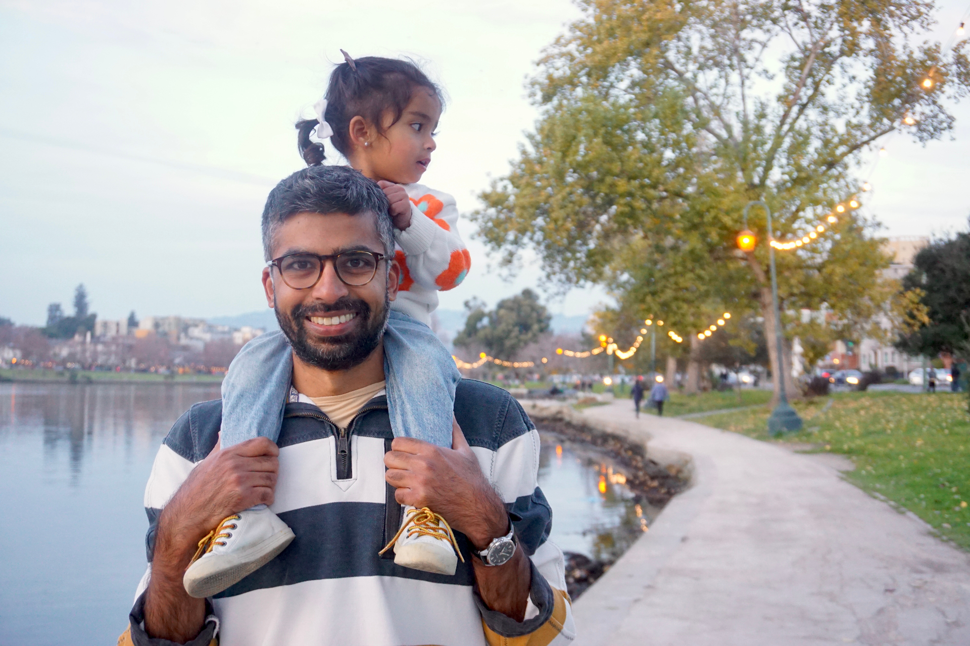The Ramachandran father smiling with his daughter on his shoulders along the Lake Merritt path strung with festival lights