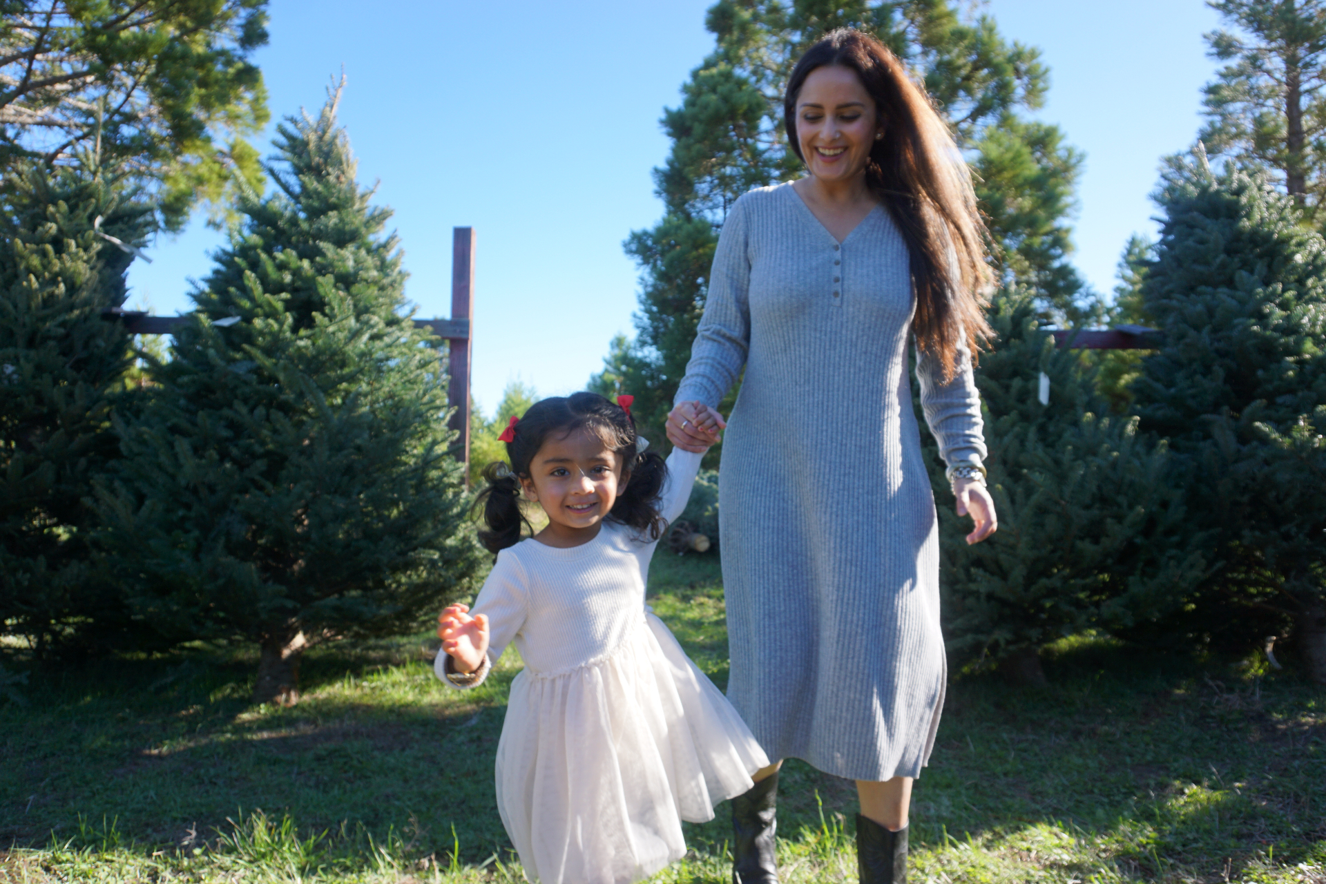 The Ramachandran mother and daughter holding hands and walking together through a Christmas tree farm on a sunny day