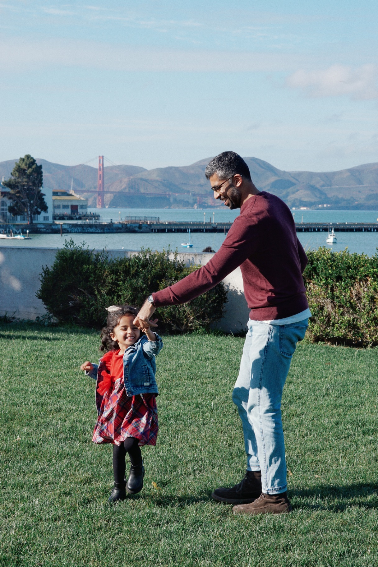 The Ramachandran father twirling his laughing daughter on the grass with the Golden Gate Bridge in the background