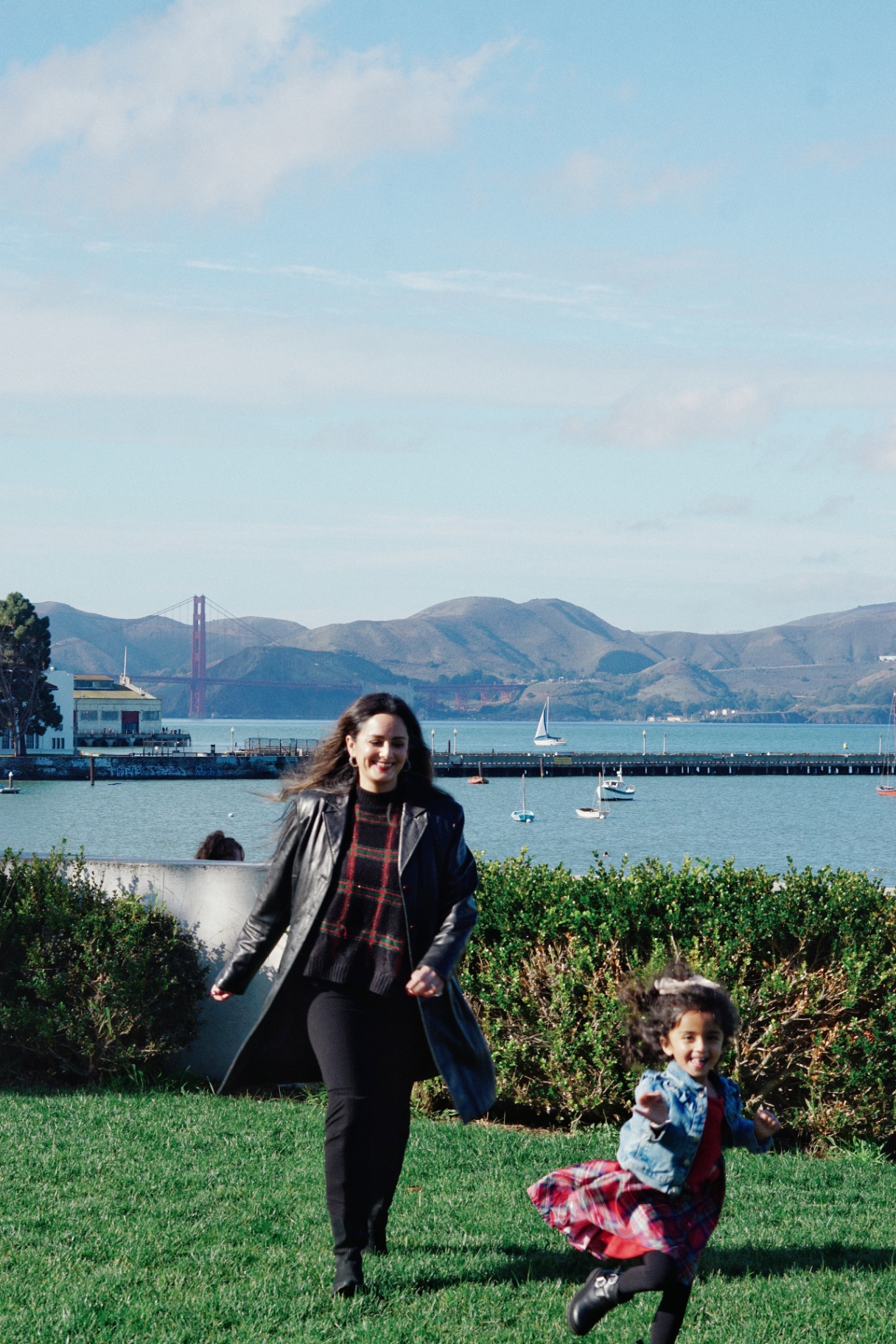 The Ramachandran mother and daughter running across the grass with the Golden Gate Bridge and bay in the background