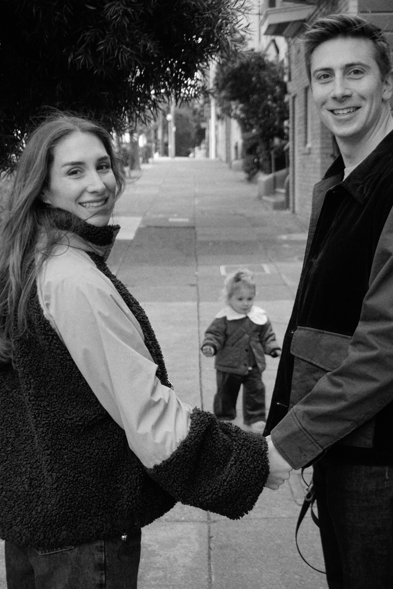 Black and white portrait of The Testa parents holding hands with their daughter walking between them on a San Francisco street