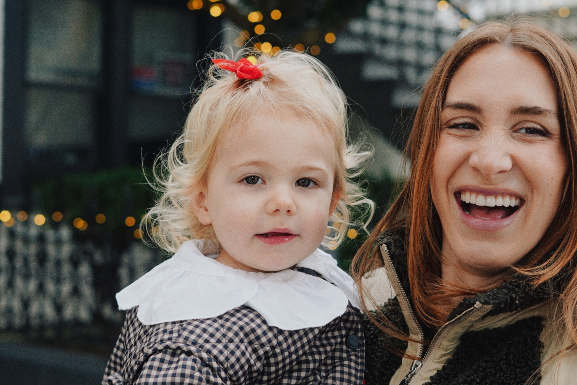 The Testa mother and daughter laughing together in front of twinkling string lights