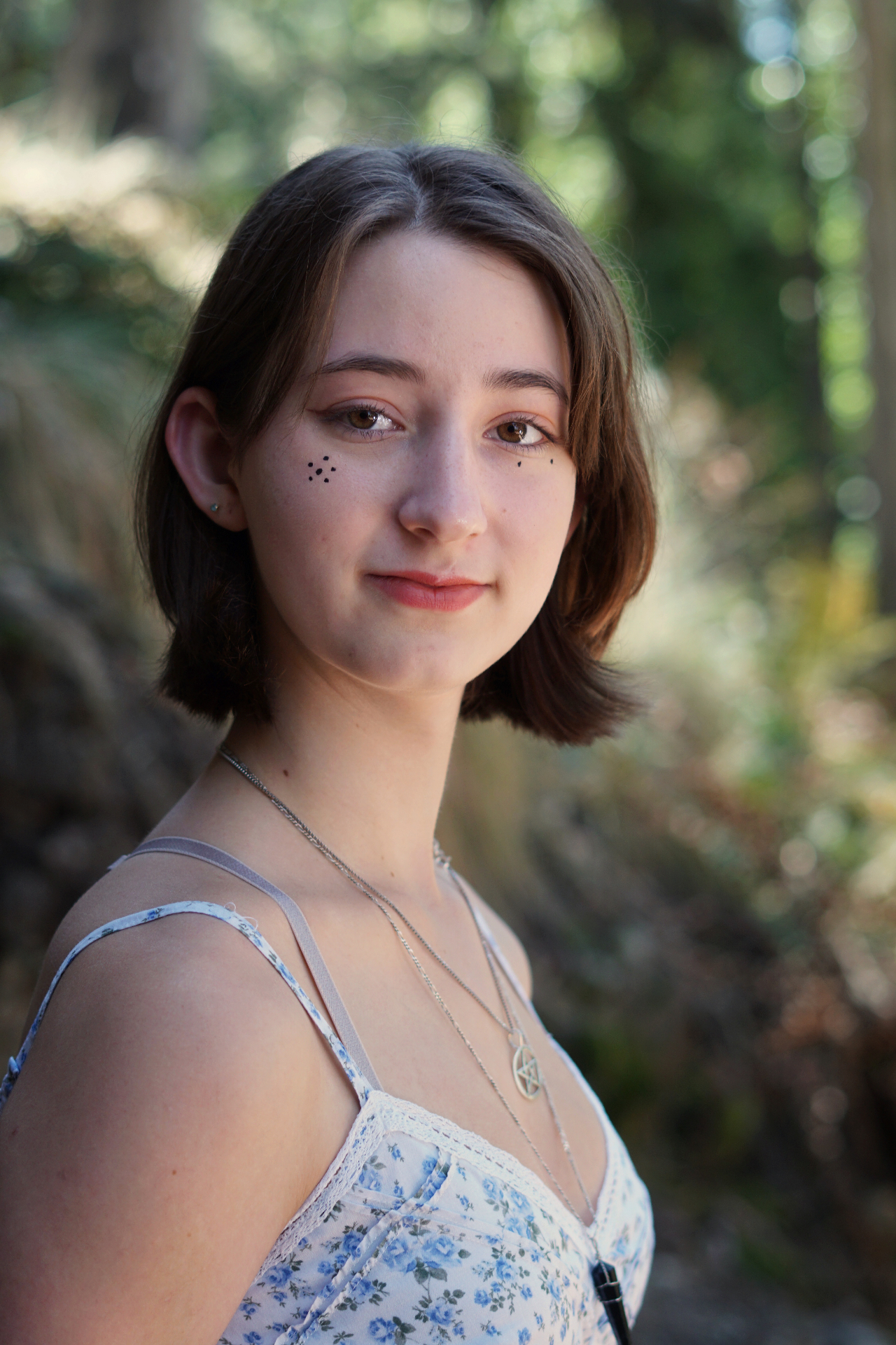 Senior portrait of The Trimble daughter softly smiling among sunlit trees