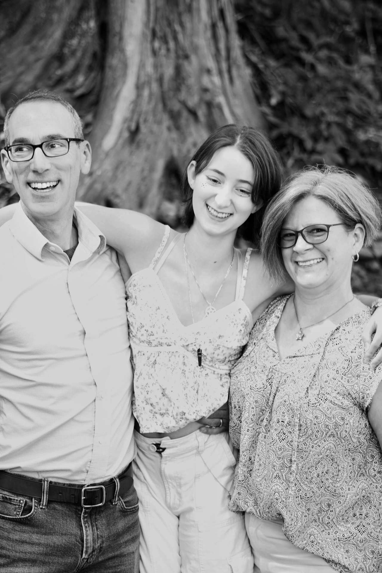Black and white portrait of The Trimble family laughing together in front of a large tree trunk